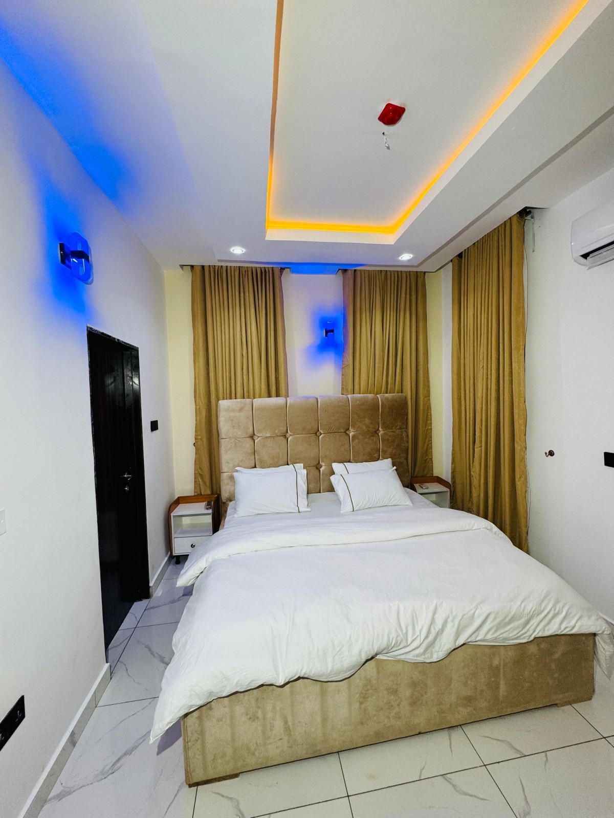 A bedroom with a buttoned gold headboard and white bedding